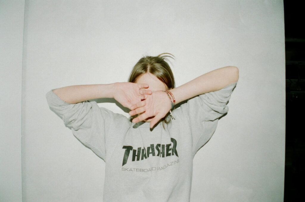 Person wearing a Thrasher sweatshirt covering face, casual and relaxed style.