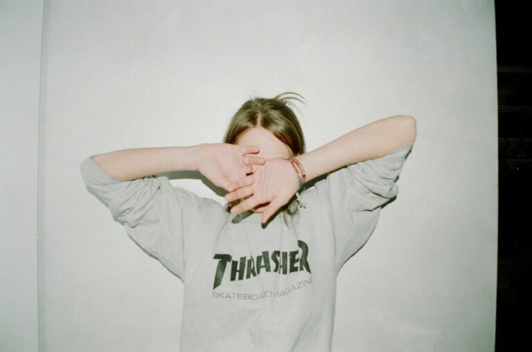 Person wearing a Thrasher sweatshirt covering face, casual and relaxed style.