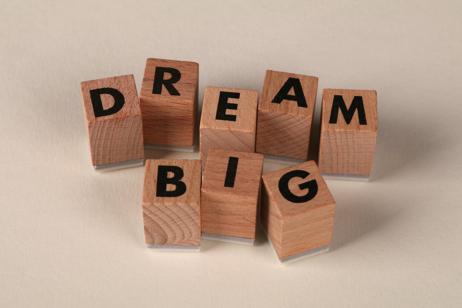 Inspiring arrangement of wooden blocks spelling 'Dream Big' on a neutral beige background.