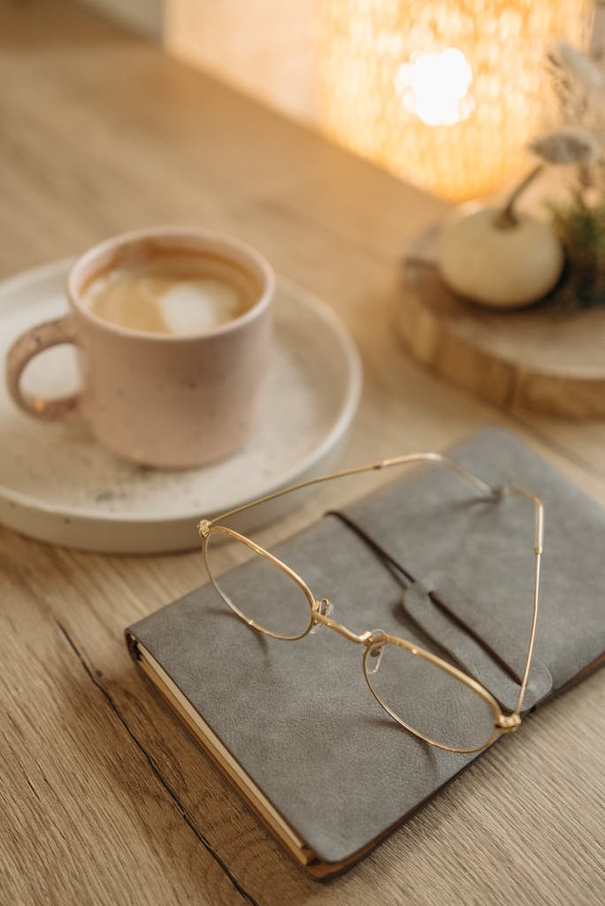Warm cozy scene featuring a latte, notebook, and eyeglasses on a wooden table.